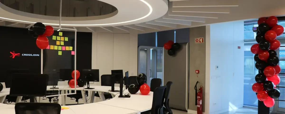 Bright open office space featuring a large circular white desk with computers, black office chairs, and festive red and black balloons.