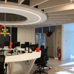 Bright open office space featuring a large circular white desk with computers, black office chairs, and festive red and black balloons.
