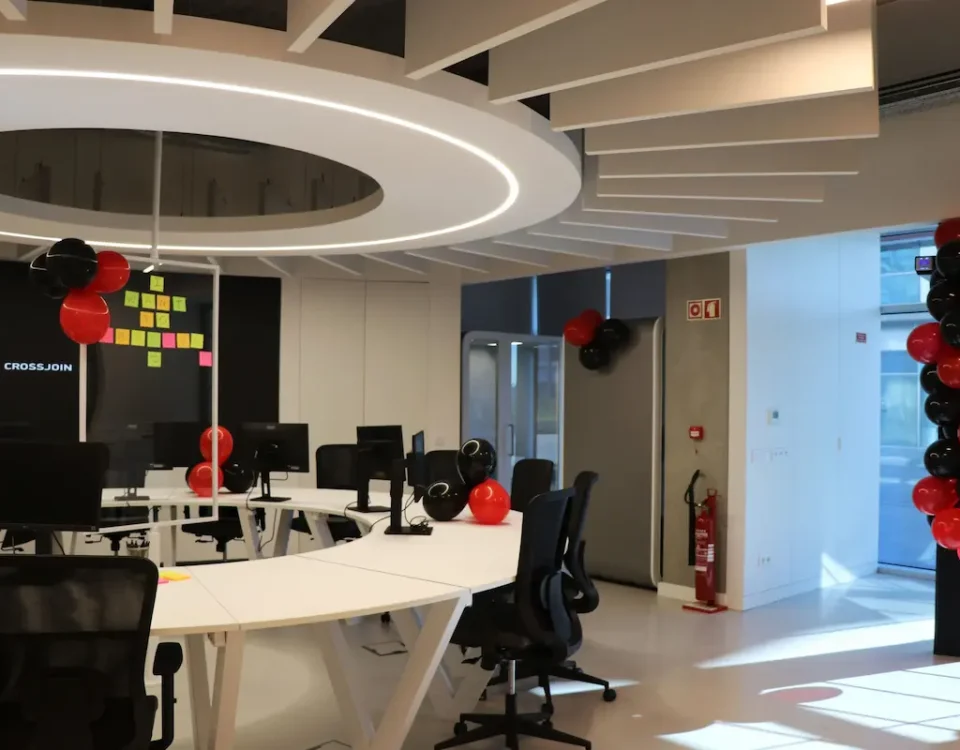 Bright open office space featuring a large circular white desk with computers, black office chairs, and festive red and black balloons.